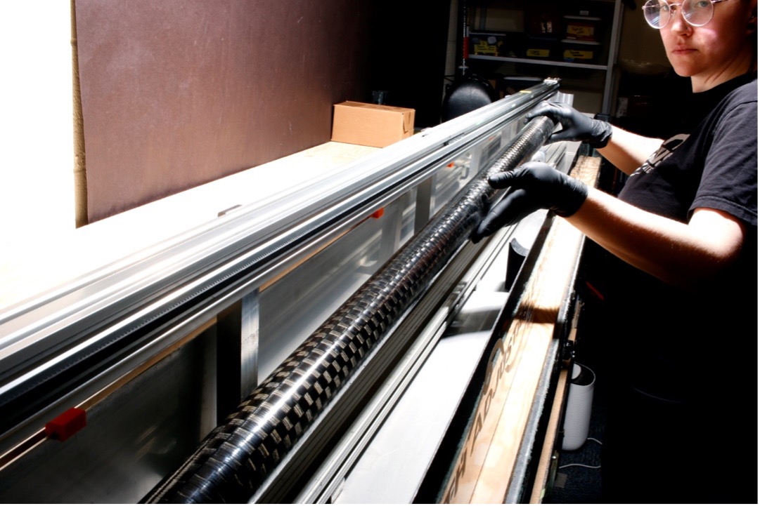 检测人员正在将一个碳纤维管放入用于检测管子的水浸槽中。