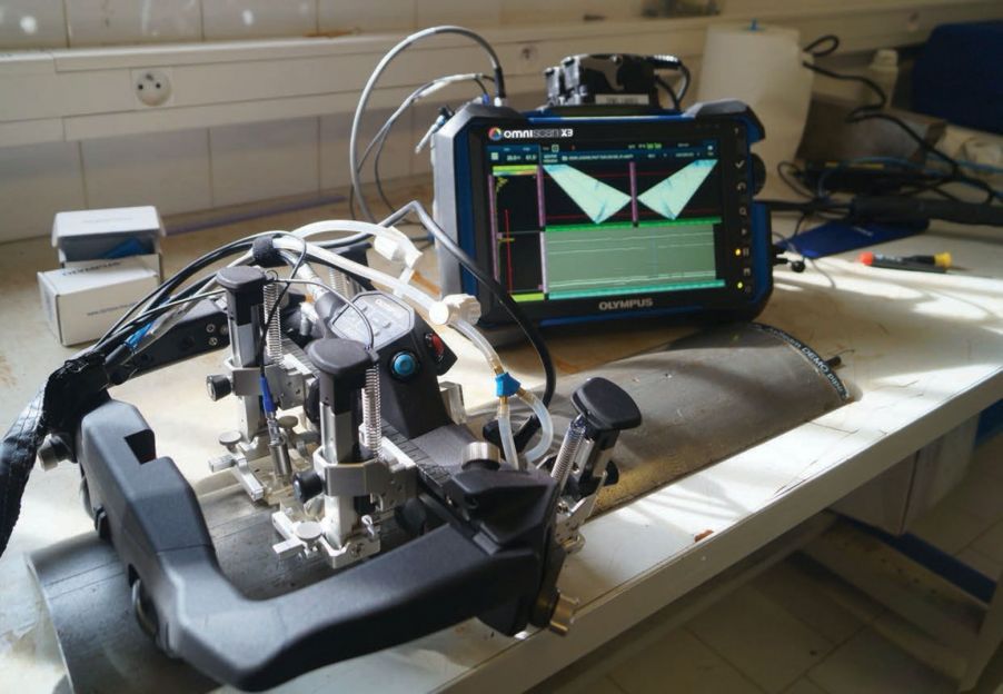 奥林巴斯AxSEAM管道纵缝扫查器放置在一个带有纵向焊缝、（纵向切割的）半管标准试块上；OmniScan X3相控阵探伤仪提供全矩阵捕获（FMC）和全聚焦方式（TFM）功能。