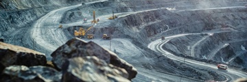Open pit mine with mining equipment including trucks and excavator in the distance.