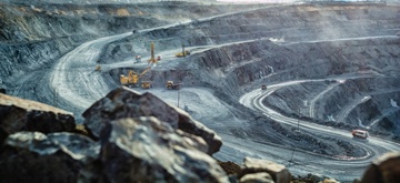 Open pit mine with mining equipment including trucks and excavator in the distance.