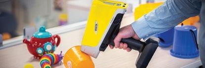 A hand holding a Vanta Max 55 kV analyzer on a plastic child’s cup testing it for RoHS compliance.